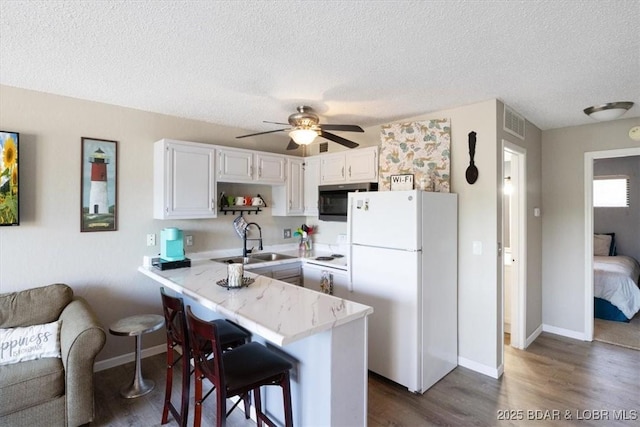 kitchen with white refrigerator, sink, white cabinetry, a kitchen breakfast bar, and kitchen peninsula