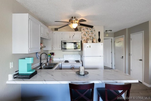 kitchen with white appliances, kitchen peninsula, a breakfast bar, white cabinets, and sink