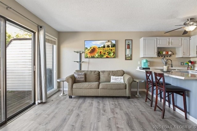 living room with a textured ceiling, ceiling fan, light hardwood / wood-style flooring, and sink