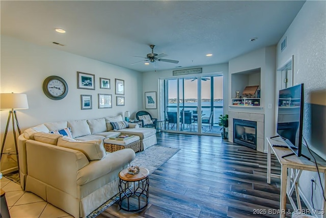 living room featuring ceiling fan, wood-type flooring, and a tiled fireplace