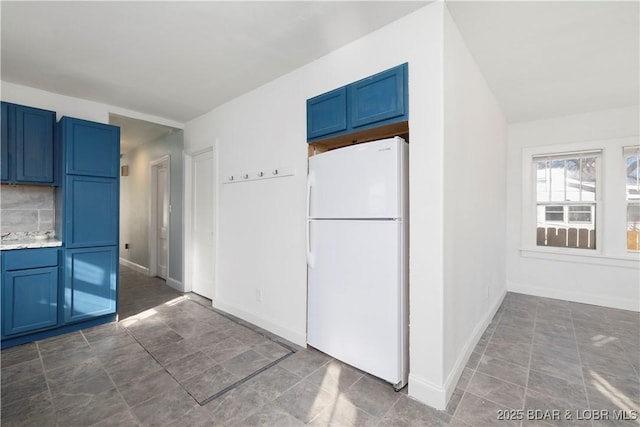 kitchen with white refrigerator, blue cabinetry, and tasteful backsplash