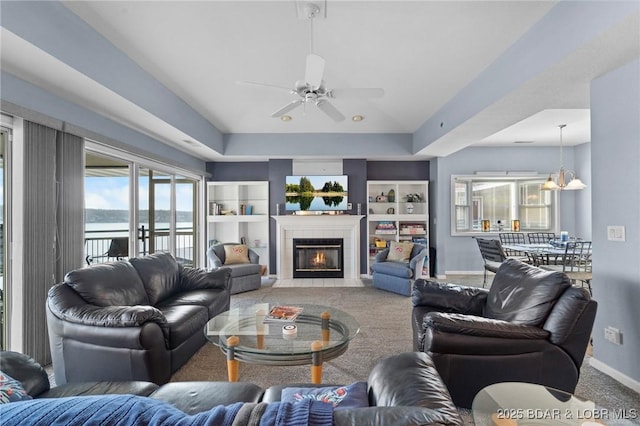 carpeted living room with ceiling fan with notable chandelier, a fireplace, built in shelves, and french doors