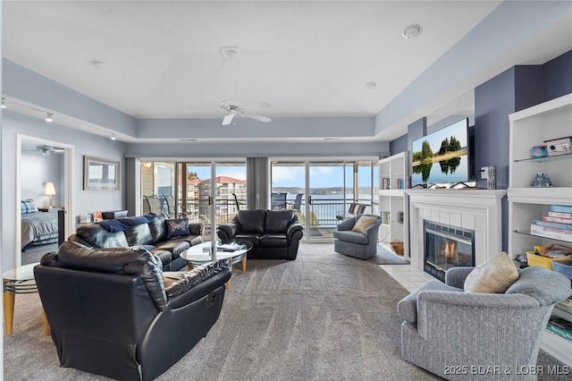 living room with ceiling fan, light colored carpet, and a tiled fireplace