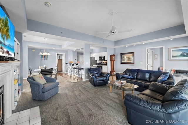 living room featuring a raised ceiling and ceiling fan with notable chandelier