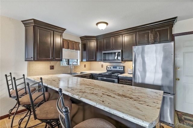 kitchen with sink, a kitchen breakfast bar, stainless steel appliances, light stone countertops, and dark brown cabinets