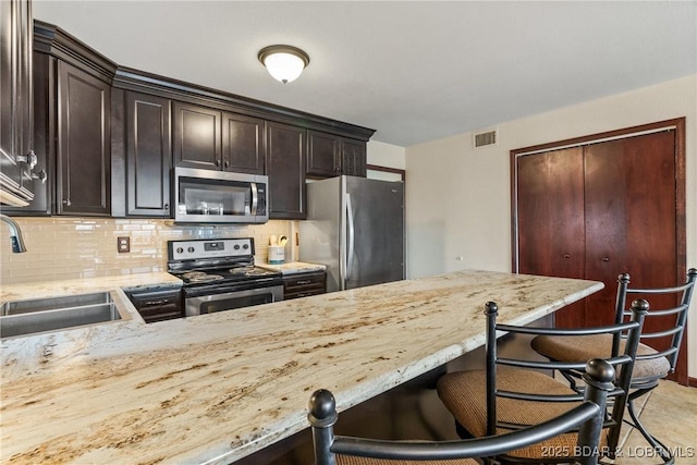 kitchen featuring appliances with stainless steel finishes, sink, backsplash, a kitchen breakfast bar, and dark brown cabinetry