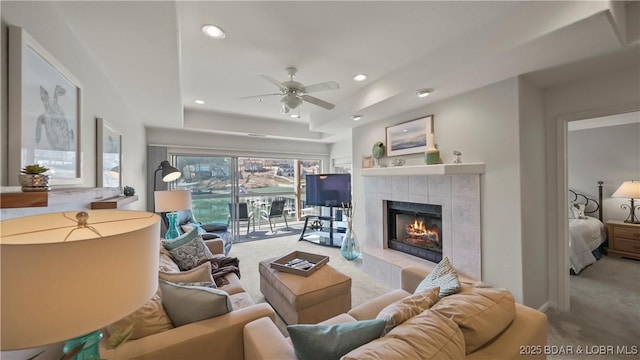 living room featuring light carpet, a fireplace, ceiling fan, and a tray ceiling