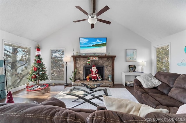 living room with a textured ceiling, lofted ceiling, ceiling fan, hardwood / wood-style flooring, and a stone fireplace