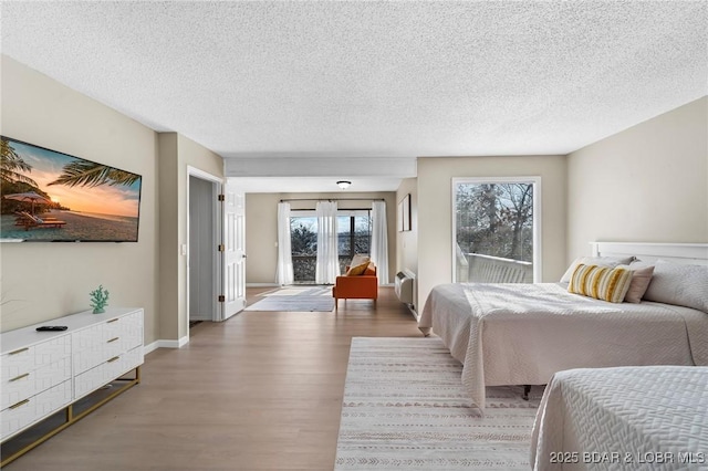 bedroom with a textured ceiling, access to outside, and hardwood / wood-style floors