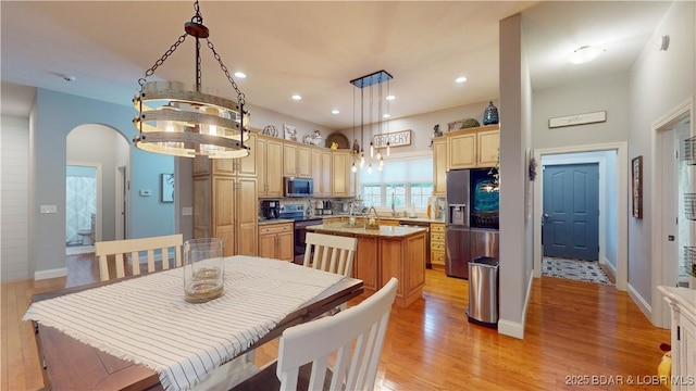 dining space with light wood finished floors, baseboards, arched walkways, and recessed lighting