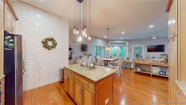 kitchen with light stone counters, decorative light fixtures, light hardwood / wood-style flooring, stainless steel refrigerator, and a kitchen island