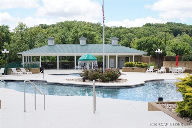 pool with a gazebo, fence, a wooded view, and a patio