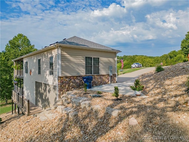 view of side of home featuring stone siding, roof with shingles, and a patio area