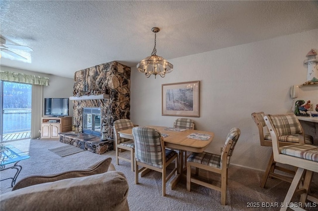 dining room featuring ceiling fan with notable chandelier, a textured ceiling, carpet floors, and a stone fireplace