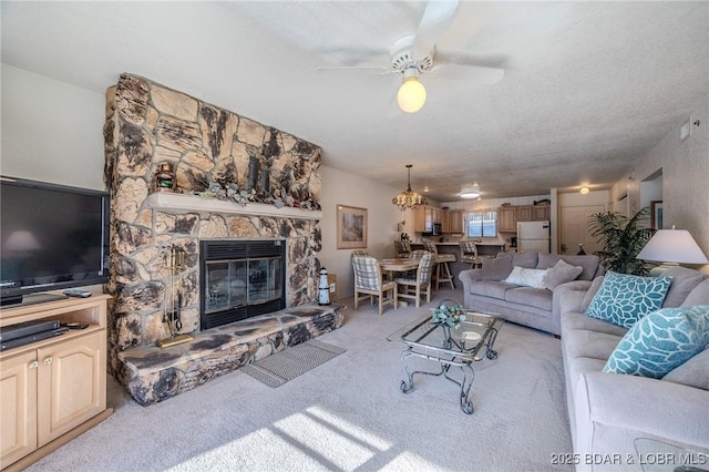 carpeted living room featuring ceiling fan with notable chandelier, a stone fireplace, and a textured ceiling