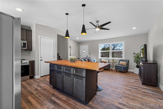 kitchen with wood counters, ceiling fan, stainless steel appliances, dark brown cabinetry, and a center island