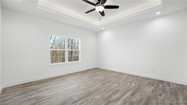 spare room with light wood-type flooring, ceiling fan, and a tray ceiling