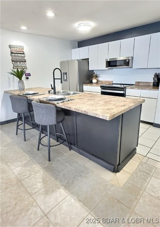 kitchen with white cabinetry, stainless steel appliances, a breakfast bar, and a kitchen island with sink