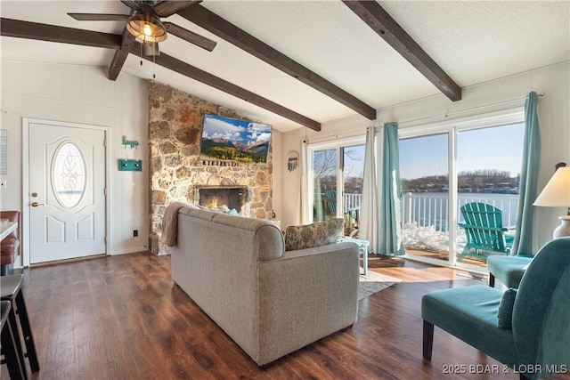 living room with ceiling fan, a fireplace, vaulted ceiling with beams, dark wood-type flooring, and a textured ceiling