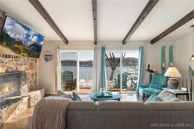 living room featuring a textured ceiling, wood-type flooring, a stone fireplace, a water view, and beam ceiling