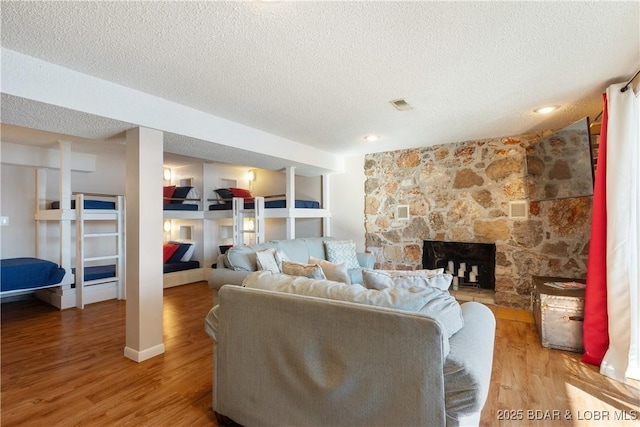 living room with wood-type flooring, a textured ceiling, and a stone fireplace