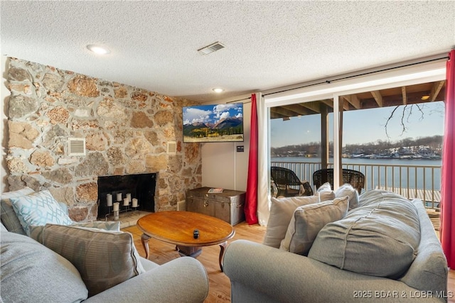 living room with a stone fireplace, a textured ceiling, and hardwood / wood-style flooring