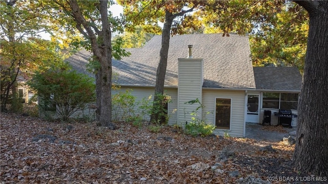 back of house with a chimney and a shingled roof