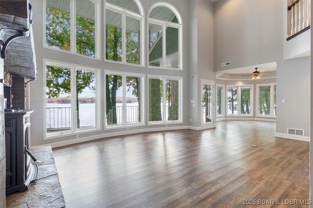 unfurnished living room with ceiling fan, a high ceiling, wood-type flooring, and a water view