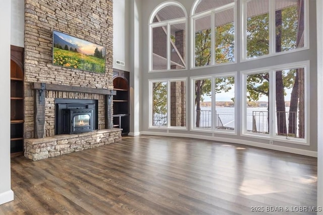 unfurnished living room with a high ceiling, dark wood-type flooring, built in features, a stone fireplace, and a water view