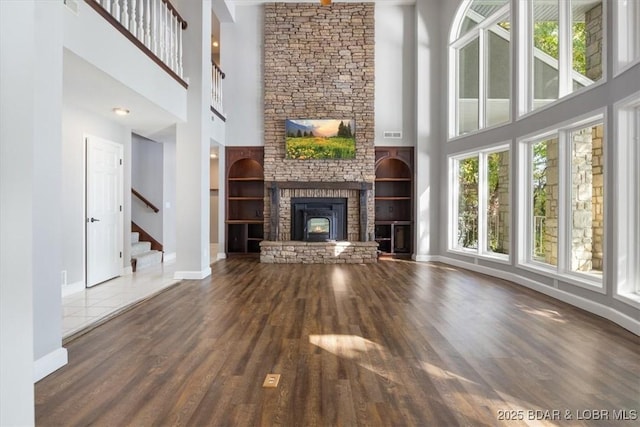 unfurnished living room with dark hardwood / wood-style flooring, a high ceiling, a stone fireplace, and built in shelves