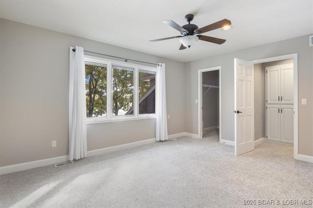 unfurnished bedroom with ceiling fan, light carpet, a closet, and a walk in closet