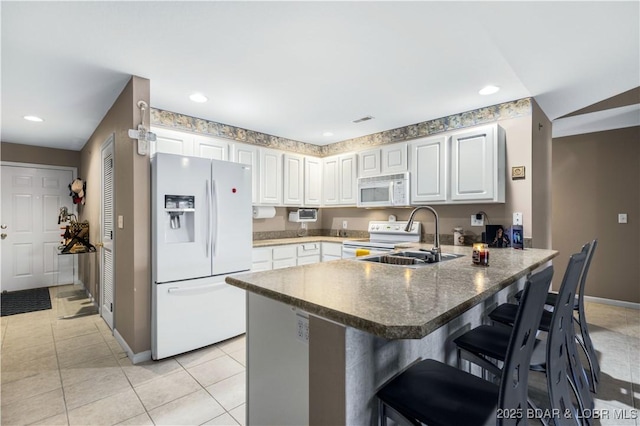 kitchen featuring a peninsula, a sink, white appliances, and baseboards