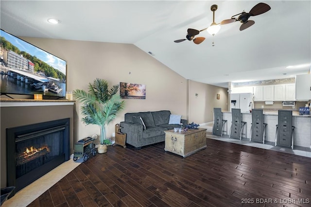 living room featuring vaulted ceiling, wood finished floors, a fireplace with flush hearth, ceiling fan, and visible vents