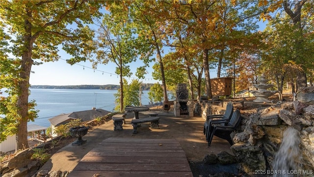 wooden terrace featuring an outdoor stone fireplace and a water view