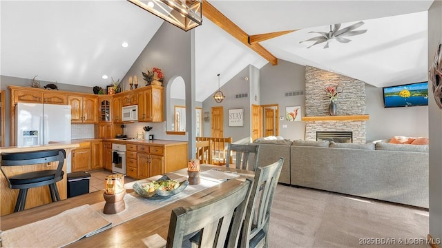 dining area with ceiling fan, beam ceiling, a fireplace, and high vaulted ceiling