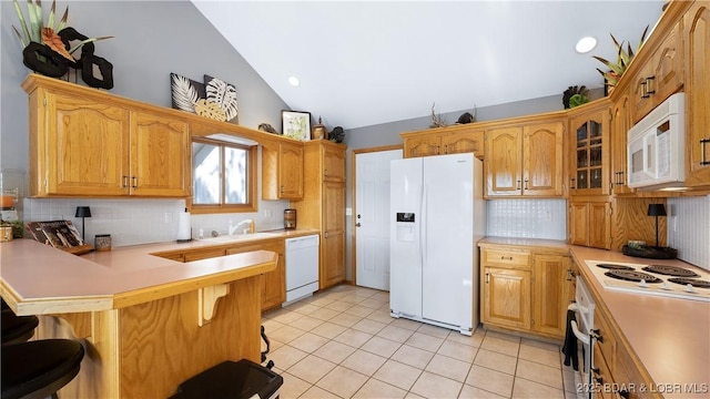 kitchen featuring vaulted ceiling, kitchen peninsula, white appliances, a kitchen breakfast bar, and light tile patterned floors