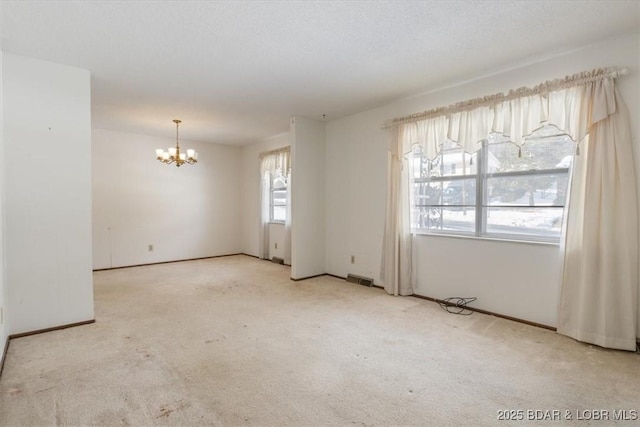 spare room featuring light carpet, a wealth of natural light, and a chandelier