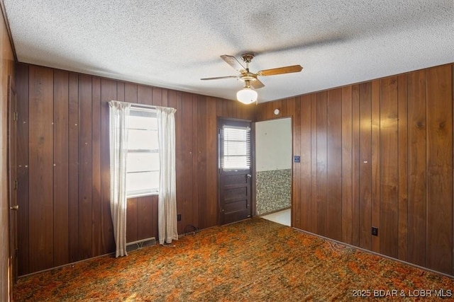 spare room featuring ceiling fan, a textured ceiling, carpet floors, and wood walls