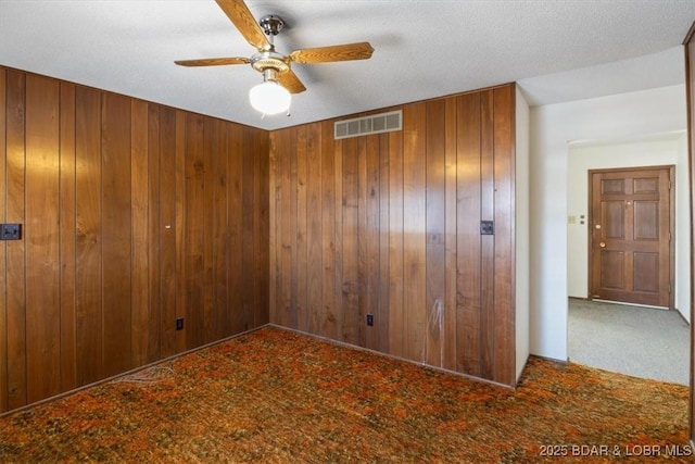 spare room featuring ceiling fan, a textured ceiling, carpet floors, and wooden walls