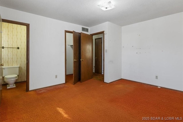 unfurnished bedroom with ensuite bath, carpet floors, and a textured ceiling