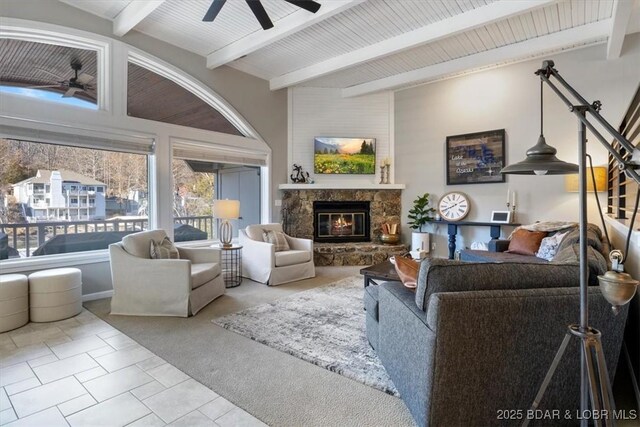 living room featuring ceiling fan, light tile patterned floors, a stone fireplace, and beamed ceiling