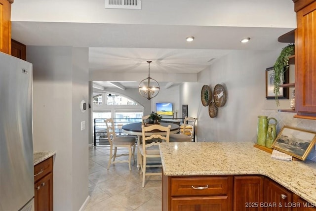 kitchen featuring light stone counters, stainless steel fridge, a chandelier, and hanging light fixtures