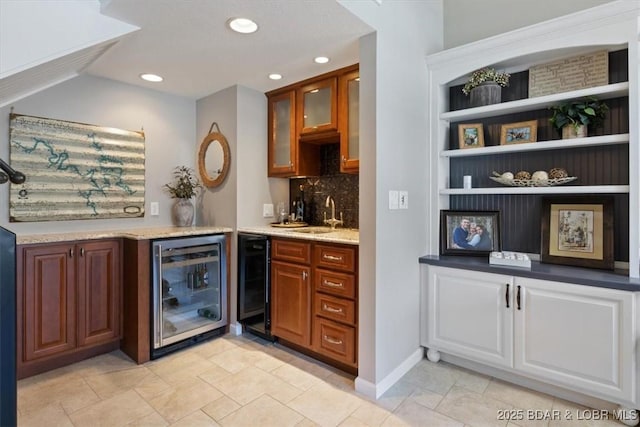 bar featuring tasteful backsplash, sink, light stone counters, and beverage cooler