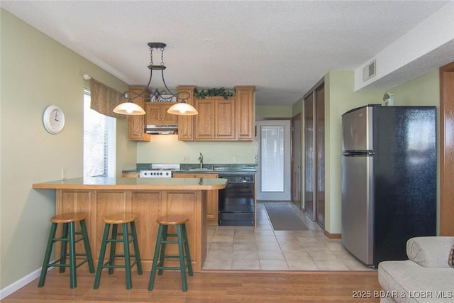 kitchen featuring stainless steel refrigerator, dishwasher, sink, a kitchen breakfast bar, and kitchen peninsula