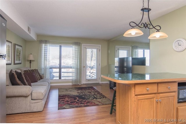 kitchen with a healthy amount of sunlight, light hardwood / wood-style flooring, a kitchen bar, and decorative light fixtures