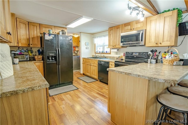 kitchen featuring kitchen peninsula, light brown cabinets, light wood-type flooring, black appliances, and sink