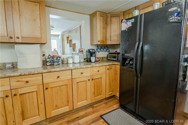 kitchen with light stone counters, light hardwood / wood-style floors, and black fridge