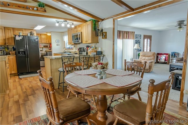 dining room with ceiling fan, sink, vaulted ceiling with beams, and light wood-type flooring