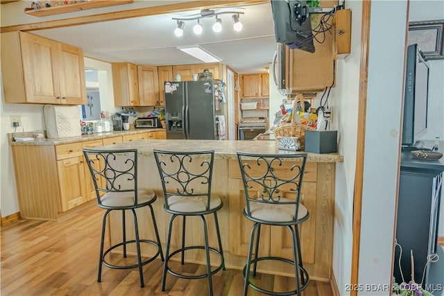 kitchen with light hardwood / wood-style floors, kitchen peninsula, light brown cabinets, black fridge, and a kitchen breakfast bar