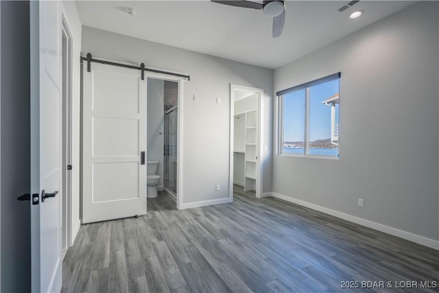 unfurnished bedroom featuring a walk in closet, connected bathroom, hardwood / wood-style flooring, ceiling fan, and a barn door